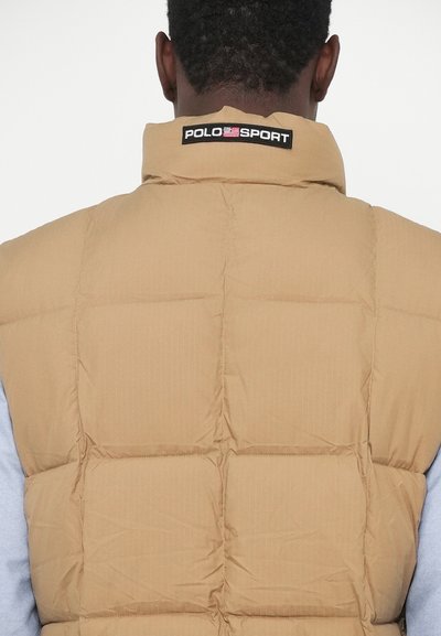 Gilet puffer beige con motivo trapuntato, dotato di un collo alto e logo "POLO SPORT" sul retro. Il tessuto appare liscio con strisce sottili.
