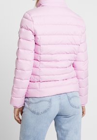 Helles rosa, puffy Jacke mit vertikal gestepptem Muster, hohem Kragen und elastischen Bündchen. Kombiniert mit hellblauen Jeans.