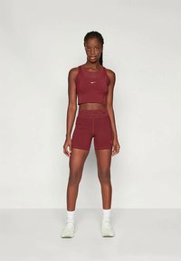 Kahvi raudonos sportinis trumpas topas su mažu logotipu, derinamas su atitinkančiomis aukšto liemens šortais. Savybės: lygus tekstūra ir prigludusi konstrukcija.