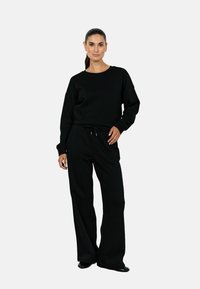 Hanorac negru cu decolteu rotund și mâneci lungi, asortat cu pantaloni largi negri din material similar, cu talie ajustabilă prin șnur. Textură netedă.