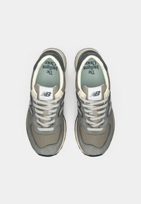 Sneaker New Balance grigie realizzate in mesh e suede, con punta tondeggiante, intersuola crema a contrasto e dettagli argentati del logo.