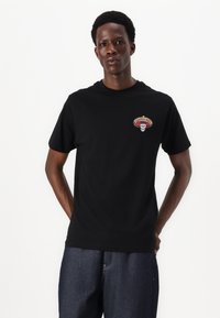 Schwarzes Baumwoll-T-Shirt mit kurzen Ärmeln, das auf der linken Brust ein mehrfarbiges Grafik-Patch mit einem Schädel unter einem Sombrero zeigt.
