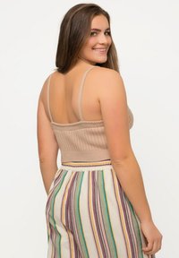 Beige žebrovaný crop top s širokými ramínky, kombinovaný s pruhovanými kalhotami širokého střihu v pastelových barvách. Top má texturovaný design.