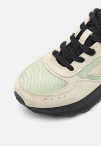 Basket avec un dessus en maille vert clair, des superpositions en daim crème et des lacets noirs. Elle possède une semelle extérieure en caoutchouc noir texturé et des détails de couture.
