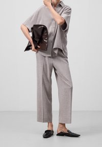 Ljust grå skjorta med krage och kort ärm, lös passform; matchande ljusgrå byxor; glänsande mörkbrun clutch; svarta slip-on skor.