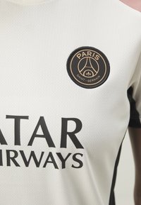 T-shirt pour homme à manches courtes en blanc, avec un tissu texturé. Détails noirs et roses et un logo rond avec "PARIS" et "SAINT-GERMAIN."