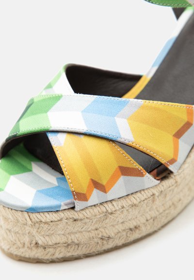 Gros plan d’une sandale compensée avec des brides en tissu géométrique multicolore et une semelle plateforme en corde tressée.