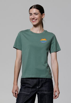 T-shirt en coton vert avec un col rond et des manches courtes, décoré d'un graphique de lèvres multicolores sur la poitrine gauche.