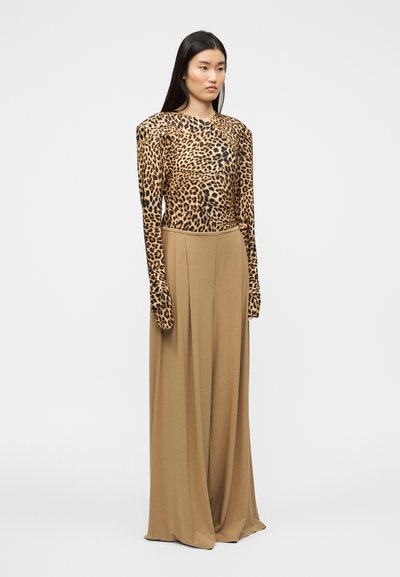 Μπλούζα με λεοπάρ μοτίβο και μακριά μανίκια με ενισχυμένους ώμους, συνδυασμένη με μπεζ παντελόνι ψηλόμεσο, φαρδύ. Ομαλή, απαλή υφή υφάσματος.