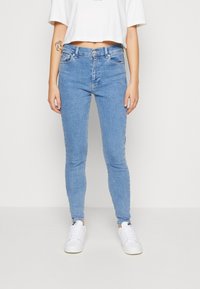 Jeans ajustados de color azul claro, confeccionados en denim, con una cintura alta, bolsillos frontales y detalles de costura sutiles, con una textura suave.