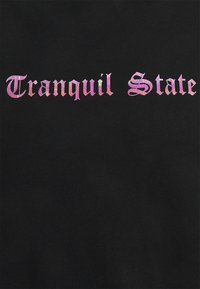 Svart tyg med en smidig textur som har texten "Tranquil State" i en gradient av rosa och lila, i en fet, serif-stil.