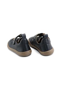 Zapatos de cuero negro con una correa ajustable, suelas de goma y detalles perforados. Forma redondeada y suela en contraste en color marrón claro.