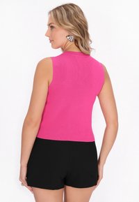 Top ajustat, fără mâneci, din material ribbed de culoare roz aprins. Spatele are un decolteu rotund și este asortat cu pantaloni scurți negri pentru un look coordonat.
