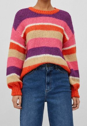 Kraftig strikket sweater med vandrette striber i orange, lilla, pink, beige og hvid kombineret med højtaljede blå jeans.