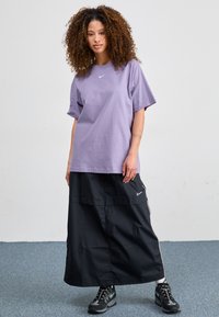 Light purple cotton t-shirt with short sleeves and a small white logo, paired with a black, knee-length, windbreaker skirt and black shoes.