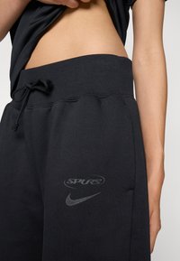 Sorte joggebukser med ribbestrikket linning og snor. Har "SPURS" og Nike-logoer i grått. Laget av myk, teksturert stoff.