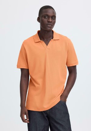 Orange polo i tekstureret stof. Har V-hals, korte ærmer og en løs pasform. Bæres med mørke jeans.