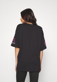 Sort bomulds t-shirt med korte ærmer og løs pasform. Har pink grafisk tekst på højre ærme. Glat tekstur, afslappet design.
