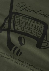 Hockeymål og puck grafik med delvis tekst på olivengrøn stofbaggrund, som fremhæver sportsudstyr og spillekontekst.