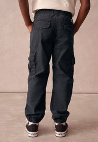 Sorte cargobukser med elastiske manchetter, baglommer og sidelommer. Kombineret med sorte og hvide Converse-sneakers.