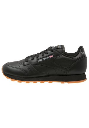 Zapatilla de cuero negra con una textura suave, que presenta cordones negros, una suela de goma naranja y acentos del logo de Reebok.