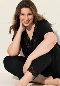 Tuta nera con dettagli in pizzo a V, maniche corte e accenti in pizzo all'orlo corto. Tessuto liscio con un fit rilassato.