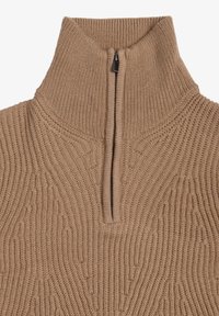 Beige strikket sweater med høj krave og en lynlås på kvart længde, der har struktureret lodret ribbede elementer og subtile dekorative mønstre.