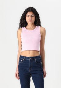 Svijetloružičasti kratki top s rebrastom teksturom, okruglim izrezom i bez rukava, u kombinaciji s tamnoplavim trapericama visokog struka.