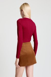 Chemise bordeaux à manches longues avec une texture côtelée, associée à une mini-jupe en daim marron, mettant en valeur des lignes simples et une silhouette ajustée.