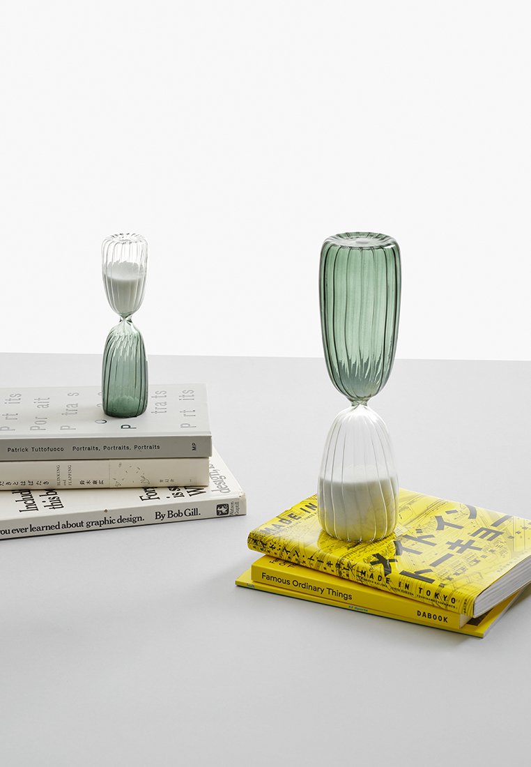 Due vasi di vetro con texture a righe; uno verde e uno bianco. Posizionati su libri impilati con diverse copertine e colori su una superficie chiara.