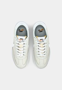 Baskets en suède blanc avec panneaux texturés, bout rond, lacets blancs et accents orange. Comprend une languette de marque et une doublure intérieure douce.