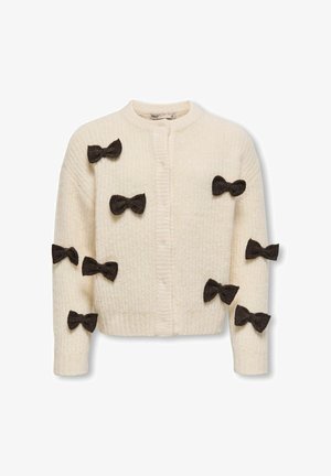 Bijela pletiva kardigan s teksturiranim materijalom i višestrukim tamnosmešnim mašnama na prednjem delu i rukavima. Okrugli izrez, zatvaranje na dugmiće.