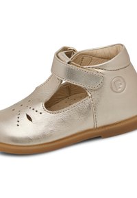 Zapato de cuero dorado con detalles recortados, una correa alrededor del tobillo y una suela marrón. Presenta un logo en relieve en el lateral.