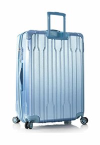 Blauer Hartschalenkoffer mit vertikalen Rillen, ausziehbarem Griff, vier Rädern und Reißverschluss. Glatte, reflektierende Oberfläche, robuste Ecken.