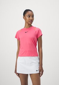 Camiseta atlética rosa de manga corta, con detalles de malla en los hombros y un logotipo negro de Nike en el pecho. Combinada con una falda blanca.