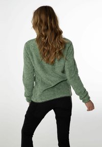 Zielony, puszysty sweter z długimi rękawami i luźnym krojem, zestawiony z dopasowanymi czarnymi spodniami. Wyraźnie zauważalna jest miękka tekstura.