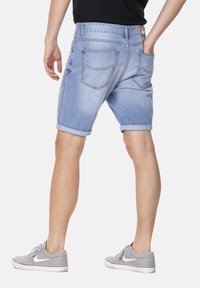 Shorts en denim bleu clair avec des revers, offrant un design de poche arrière. Portés avec des baskets grises et un t-shirt noir.