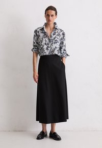 Blouse bleu clair à motifs floraux avec des accents noirs, associée à une jupe noire longue jusqu'au sol, dotée de poches latérales et d'une texture lisse.