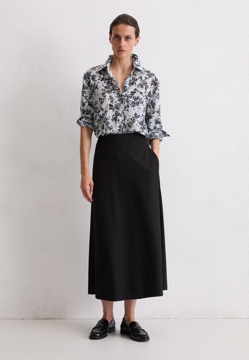 Blouse bleu clair à motifs floraux avec des accents noirs, associée à une jupe noire longue jusqu'au sol, dotée de poches latérales et d'une texture lisse.