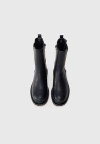 Black leather ankle boots with a smooth finish, rounded toe, and flat sole. Side zip fasteners and pull tabs for easy wear.