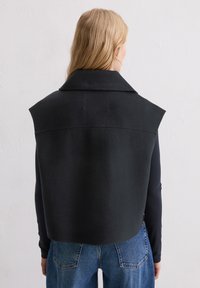 Czarna kamizelka bez rękawów z szerokim kołnierzem, wykonana z fakturowanej tkaniny. Tył jest prosty i minimalistyczny, bez ozdób.