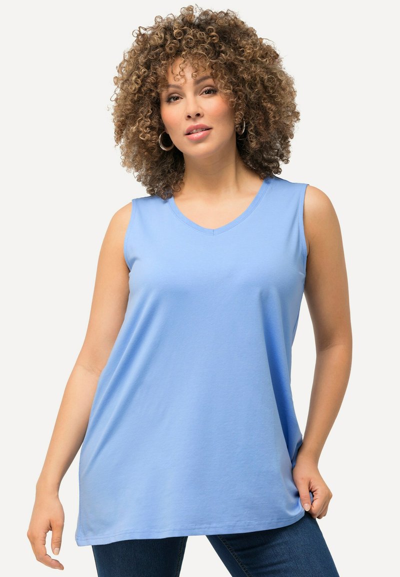 Lichtblauw mouwloos shirt met een V-hals, gemaakt van zachte stof, met een losse pasvorm en subtiele draping, gecombineerd met donkerblauwe jeans.