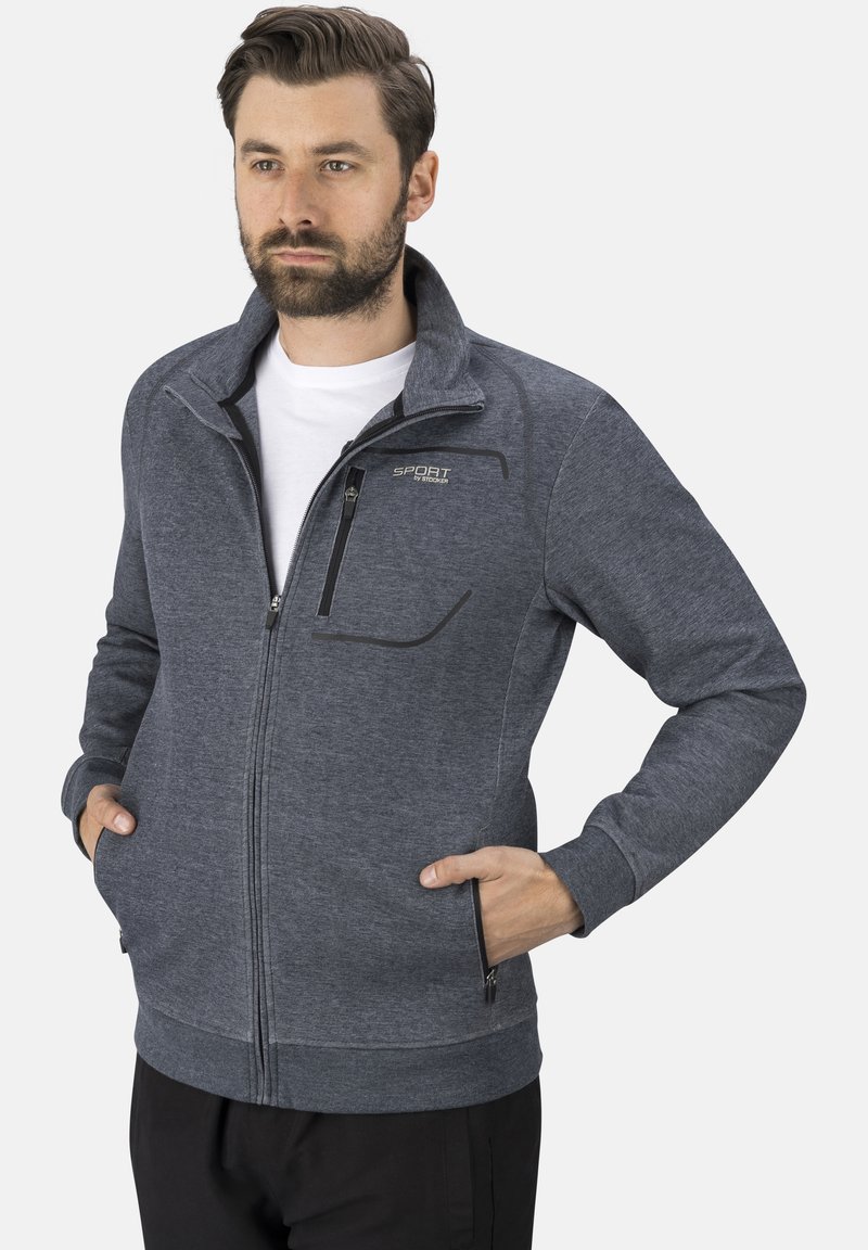 Graue Zip-Jacke aus weichem Stoff mit hohem Kragen, seitlichen Taschen und sichtbarem Logo. Sie verfügt über eine moderne, taillierte Silhouette.