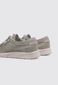 Zapatillas de ante gris con un acabado texturizado, presentando acentos claros y un leve tacón. Diseño de cordones con perforaciones sutiles para transpirabilidad.