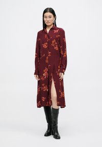 Μπορντώ φλοράλ φόρεμα με μακριά μανίκια, γιακά, πλαϊνό σκίσιμο και κεντήματα σε πορτοκαλί και ροζ. Συνδυάζεται με μαύρες μπότες μέχρι το γόνατο.