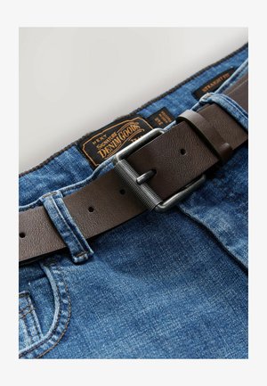 Braunger Ledergürtel mit einer silbernen Metallschnalle, befestigt an blauen Jeans aus Denim, die einen strukturierten Stoff und sichtbare Nähdetails aufweisen.