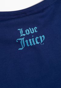 Tamsiai mėlynas medvilnės audinys su išsiuvinėtu tekstu "Love Juicy" šviesiai mėlyna spalva. Raidės stilizuotos, turi šiek tiek blizgantį tekstūrą.