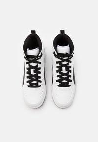 Korkeat tennarit, joissa on valkoinen nahkapinta, mustat yksityiskohdat, mustat nauhat ja pehmustettu kaulus. Silkkinen pinta, jossa on reikäkuvioita.