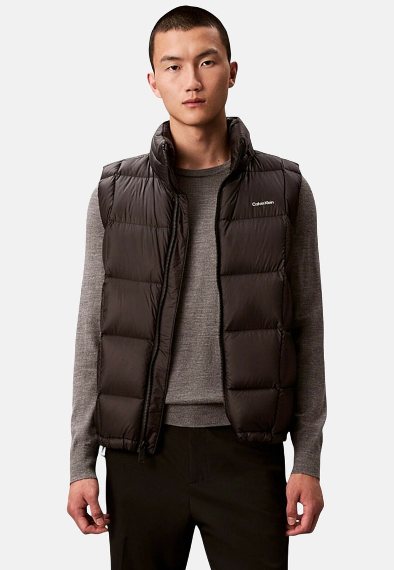 Czarna ocieplana kamizelka puchowa z wysokim kołnierzem, zamkiem błyskawicznym i logo na piersi. Posiada pikowane sekcje i gładką fakturę tkaniny.