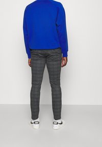 Felpa in pile blu, pantaloni grigi a quadri, sneakers bianche con accenti neri. Polsini a costine sulle maniche, vestibilità rilassata nella felpa.